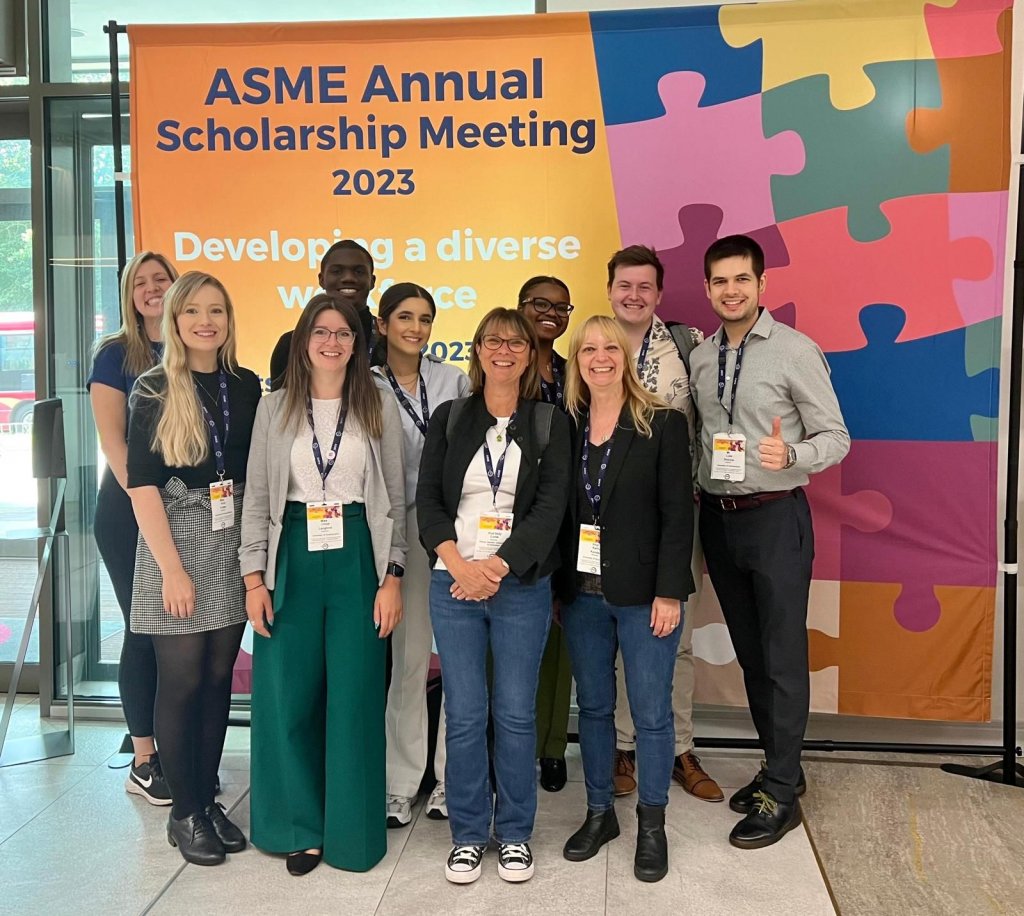Ten students and staff from the Faculty of Medicine at Southampton stand in front of a large colourful banner with the words 'ASME Annual Scholarship Meeting 2023' printed on it. The group are all smiling at the camera.